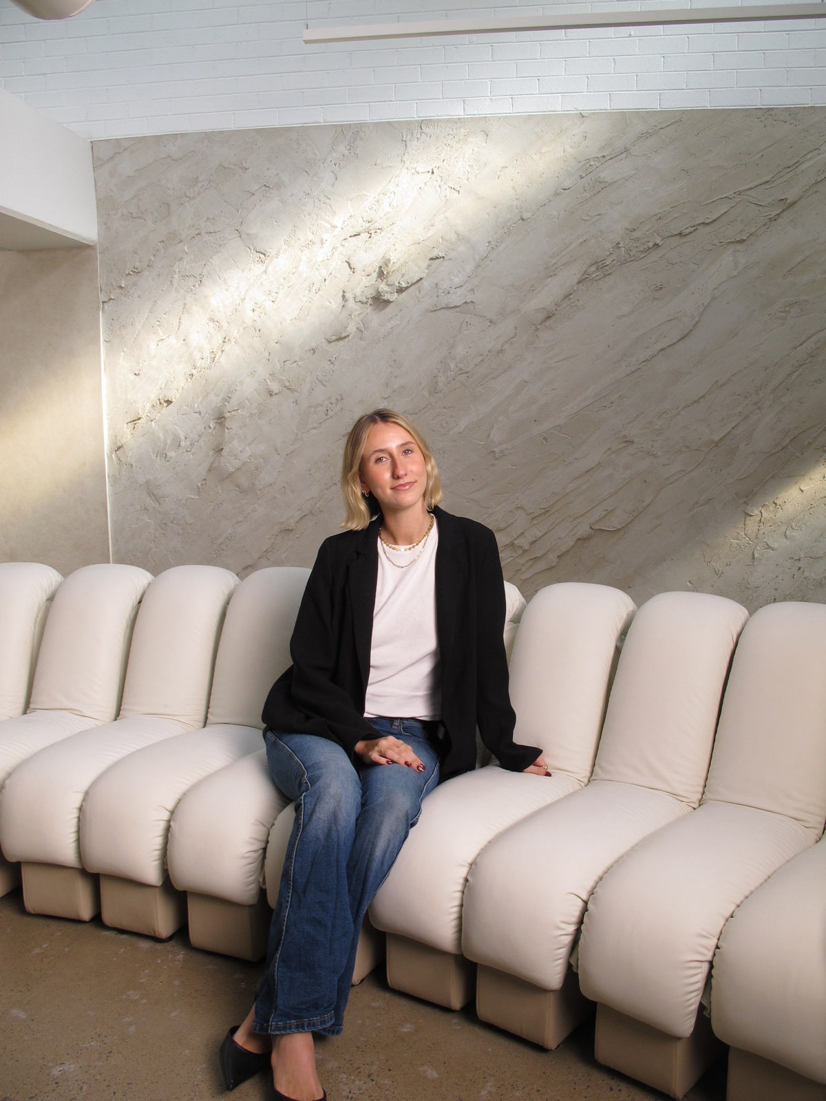 Kate seated on the cream banquette at Sœur. Skin, against the textured plaster wall