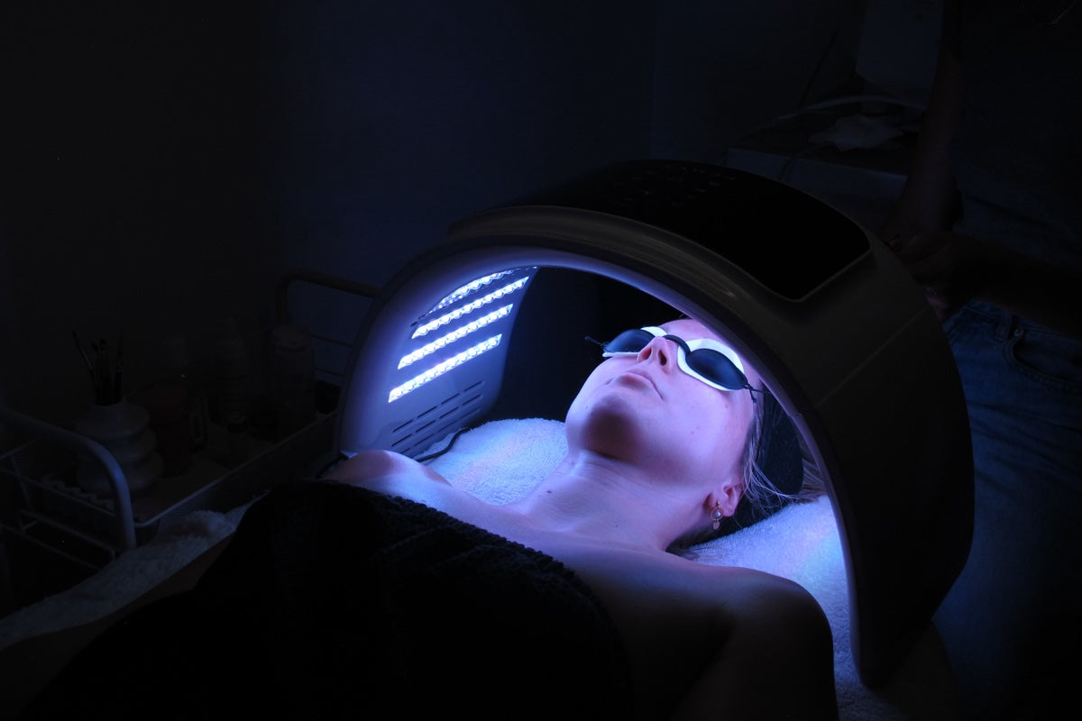 A client under the LED light therapy panel, blue light across her face