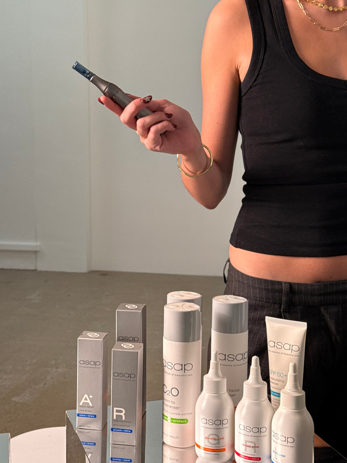 Kate holding a skin-needling pen, the ASAP range laid out in front of her