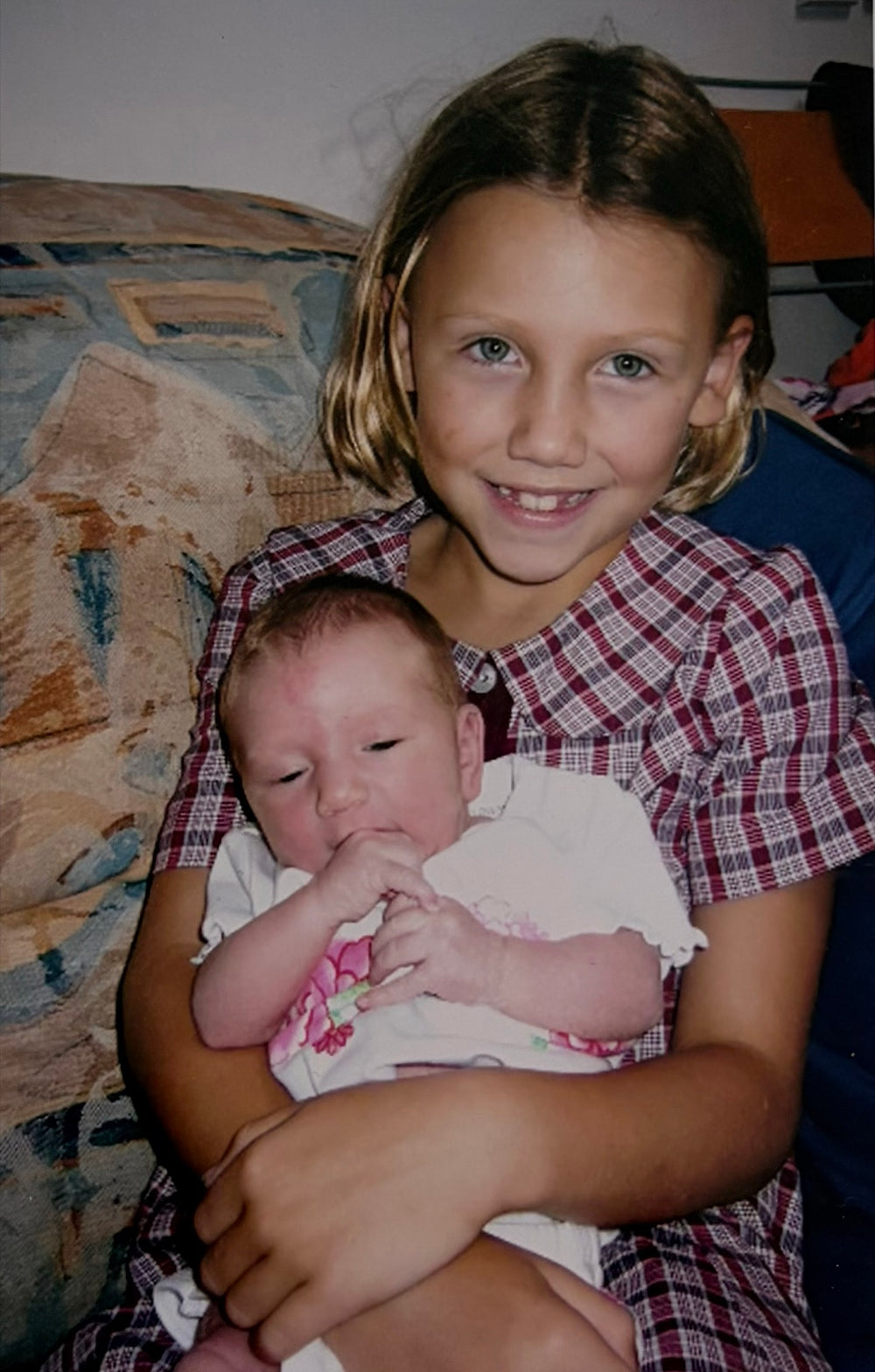 A young Annie sitting on a sofa, holding her newborn sister Kate
